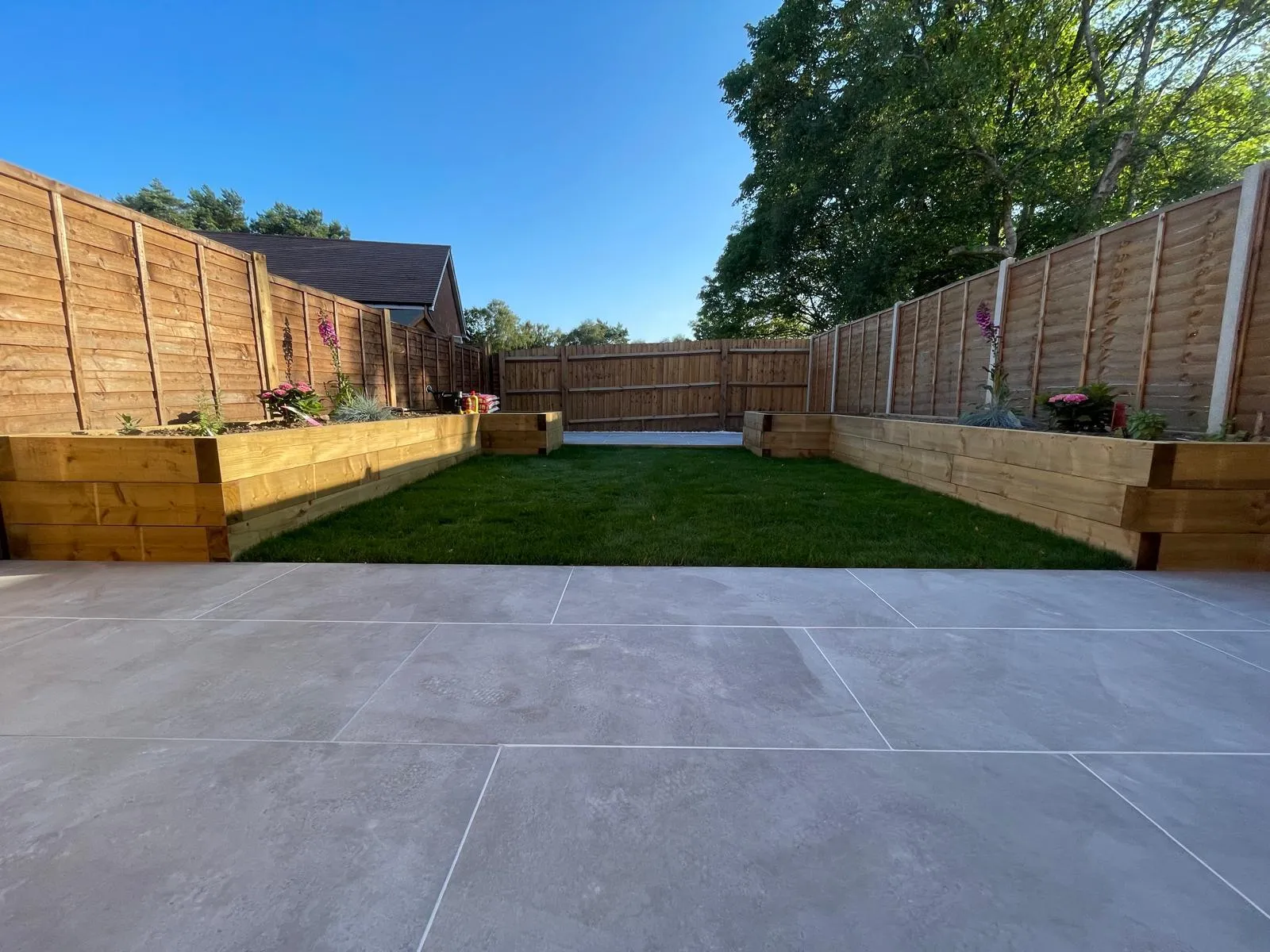 A backyard with a fence, grass and wooden planters.