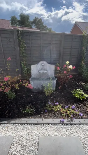A garden with flowers and a fountain in the middle of it.